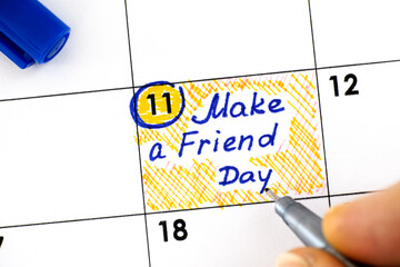 Woman fingers with pen writing reminder Make a Friend Day in calendar.