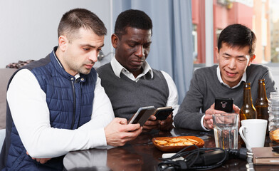 Three friends are chatting each in his phone while relaxing together at home.
