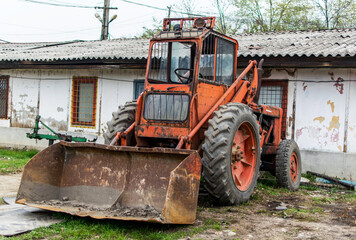 Fototapeta na wymiar Front/ grapple loader- Old industrial equipment used for loading various materials. In the background is an old abandoned warehouse