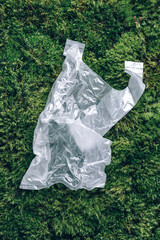Disposable plastic bag on green moss, grass background. Pollution problem concept. Top view. Copy space. Environmental pollution problem. Garbage, waste collection and sorting, trash outdoors