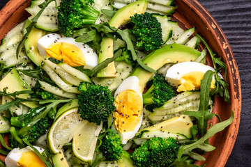 Close up Avocado salad with broccoli, cucumber and boiled eggs in a white vintage bowl. Delicious breakfast or snack
