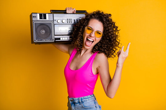 Photo of cool crazy youngster lady wavy hairdo listen youth music hold retro boom box chill beach party make finger horns wear summer pink singlet isolated vibrant yellow color background