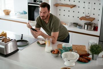 Young man eating breakfast and reading the news online. Handsome man enjoying at home.