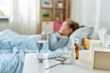 health, children and people concept - medicine on table for sick little girl lying in bed at home