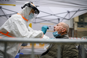 Senior man in covid-19 testing center outdoors on street, coronavirus and taking swab concept.