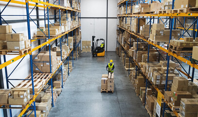 Men workers with forklift and pallet truck working indoors in warehouse, coronavirus concept.