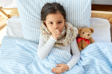 health, children and people concept - sick coughing girl lying in bed at home
