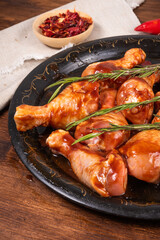 Raw chicken drumsticks marinated in spicy sauce on a black frying tray with spices, close-up