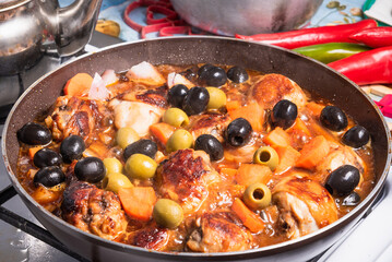 Cooking Algerian chicken with vegetables and olives with hot sauce in a pan on the stove with hot peppers