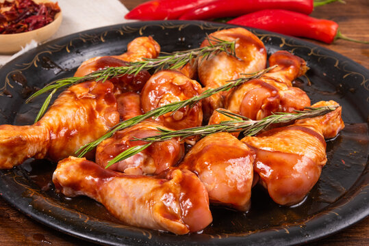 Raw chicken drumsticks marinated in spicy sauce on a black frying tray with spices, close-up