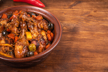 Ready Algerian tajine chicken with vegetables and olives with spicy sauce on a wooden table, top view, close-up, copy space