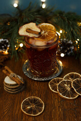 Traditional Christmas mulled wine in glass garnished with cinnamon stick and dried orange arranged on wooden table in cafe with cozy festive atmosphere 