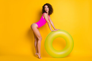 Full size profile photo of attractive barefoot lady tourist resort swim big green round circle water look side wait boyfriend join her wear pink swimsuit isolated vivid yellow color background