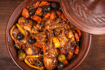 Ready Algerian tajine chicken with vegetables and olives with spicy sauce on a wooden table, top...