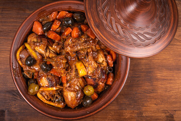 Ready Algerian tajine chicken with vegetables and olives with spicy sauce on a wooden table, top view, close-up
