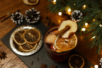 Aromatic Christmas mulled wine with slice of orange and cinnamon stick in glass on slate board in cafe prepared for celebration of winter holidays 