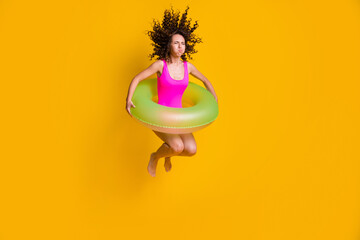 Photo portrait of young curly girl jumping into pool holding breath closed eyes with inflatable green circle wearing fuchsia swim wear isolated on vivid yellow colored background - obrazy, fototapety, plakaty
