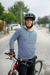 Portrait of down syndrome adult man with bicycle standing outdoors on street.