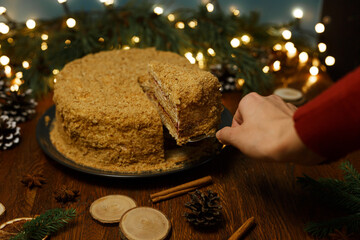 Crop woman serving delicious honey cake on table decorated and prepared for Christmas celebration in cozy room 