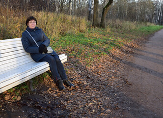 Fototapeta premium After a long walk, Natalia sat down to rest on a white bench in the park, free of strangers. 