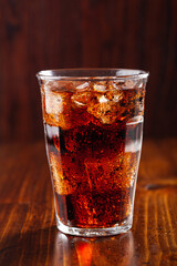 glass of cold cola soft drink with ice on wooden background