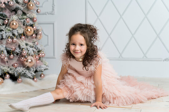 a little girl in a beautiful dress makes twine near the Christmas tree