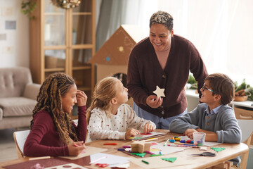 Portrait of smiling African-American woman teaching art class with multi ethnic group of children...