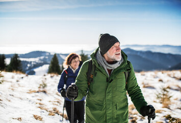 Senior couple with nordic walking poles hiking in snow-covered winter nature.