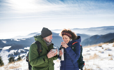 Fototapeta premium Senior couple hikers in snow-covered winter nature, drinking hot tea.