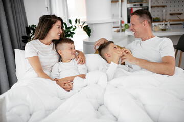 Obraz na płótnie Canvas Young family enjoying in bed. Happy parents with sons relaxing in bed...