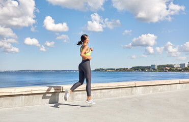 Fototapeta na wymiar fitness, sport and healthy lifestyle concept - young woman running along sea promenade