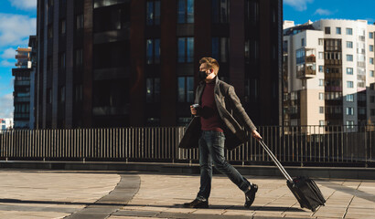 Business trip during coronavirus pandemic. Young man with luggage case against the background of...