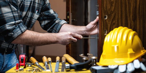 Carpenter at work repairs and installs the door lock. Carpentry.