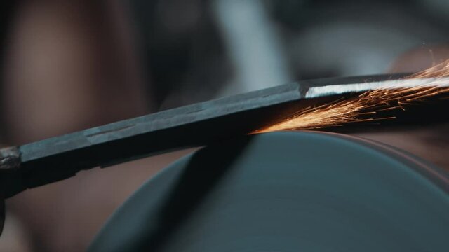 Close up of a knife sharpened on rotating machine, hot sparks flying slow motion