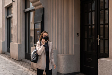 Girl walking with face mask and calling on her phone. Autumn city mood. Covid-19.