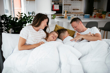 Young family enjoying in bed. Happy parents with sons relaxing in bed...