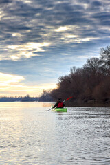 Woman kayaking on green kayak in winter Danube river at sunset. Back view. Concept: adventure, holiday, vacation