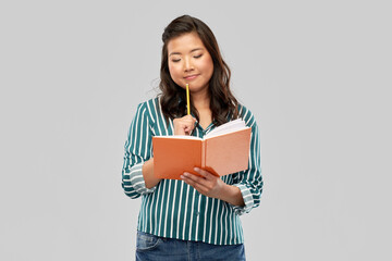 Obraz premium education, school and inspiration concept - asian student woman with diary and pencil over grey background
