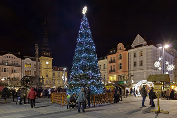 Ostrava, Czech Republic. Christmas market on Masaryk square with city's main Christmas tree in dusk. The Old Town Hall and the Marian Column are visible on the left part of the image.