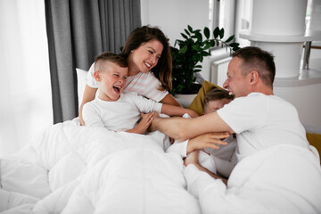 Obraz premium Young family enjoying in bed. Happy parents with sons relaxing in bed...