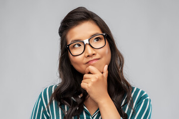 people, education and school concept - portrait of thinking asian woman in broken glasses with patch or student looking up over grey background