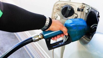 A man holding a diesel injector into a car's tank. A male worker refueling a silver bronze pickup truck with a blue nozzle in a gas station. Selective focus