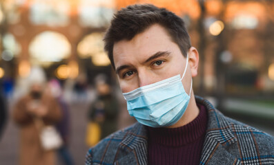 Outdoor portrait of an attractive young man in winter clothes and protective medical face mask. Prevention of Covid-19 coronavirus infection. A handsome guy on the street during a new flu epidemic.
