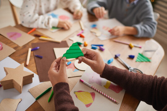Close up of unrecognizable girl holding paper Christmas tree while doing art and craft project with group of children, copy space