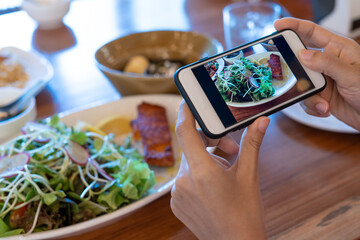 Hand of woman take photo of breakfast with a smartphone on the table. woman is use phone to take pictures of food to review or upload social media.