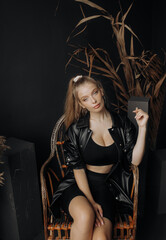 Fototapeta na wymiar Fashion blonde in a black suit posing on a straw chair on a black background.