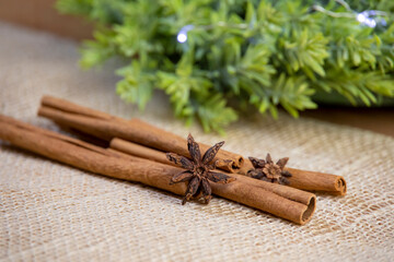 close-up of cinnamon sticks and anise, dry and raw ingredients, green wreath with lights, bright christmas decoration on jute, front view