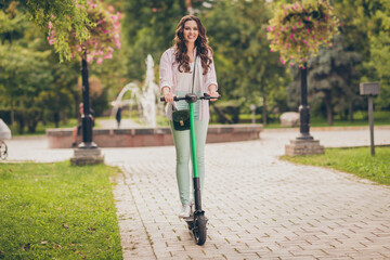 Full body photo of pretty young woman happy smile enjoy ride electric scooter spring time in park