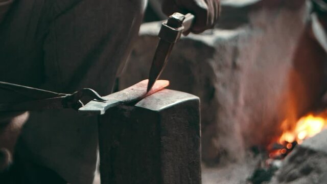 Blacksmith cutting hot steel piece with a chisel and pouring water over it