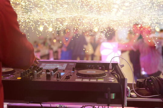 Mixing console is played by DJ and couples dancing on the dance floor in the background